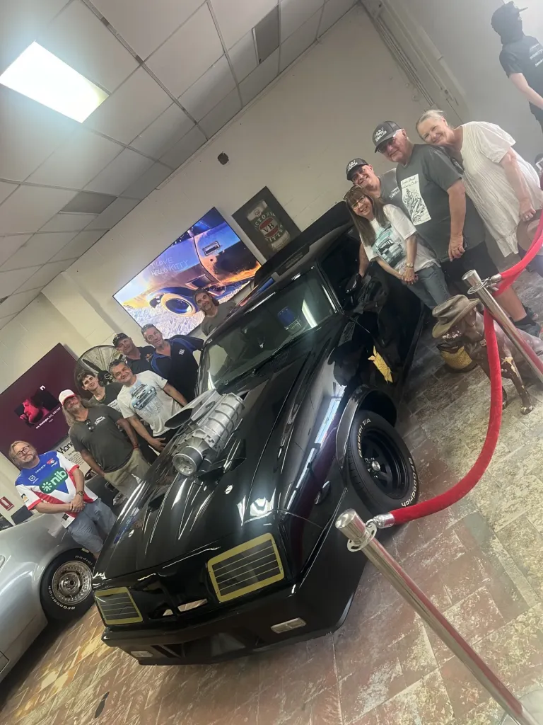 Group of visitors posing around the black Mad Max Interceptor replica inside the museum