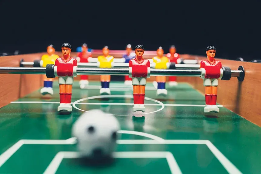 Close-up of foosball table figures in red and yellow with a white ball in the foreground