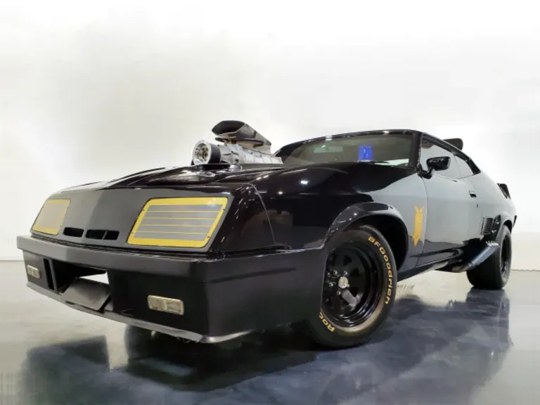 Black Mad Max Interceptor replica with a bonnet supercharger and gold headlight grilles, seen from a low angle