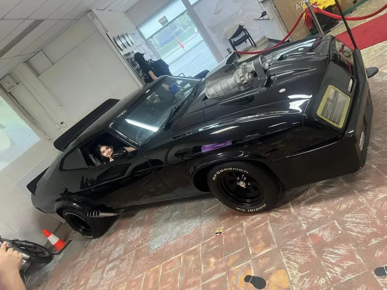 Young visitor sitting in the driver's seat of the black Interceptor replica at the sit-in-the-car photo spot