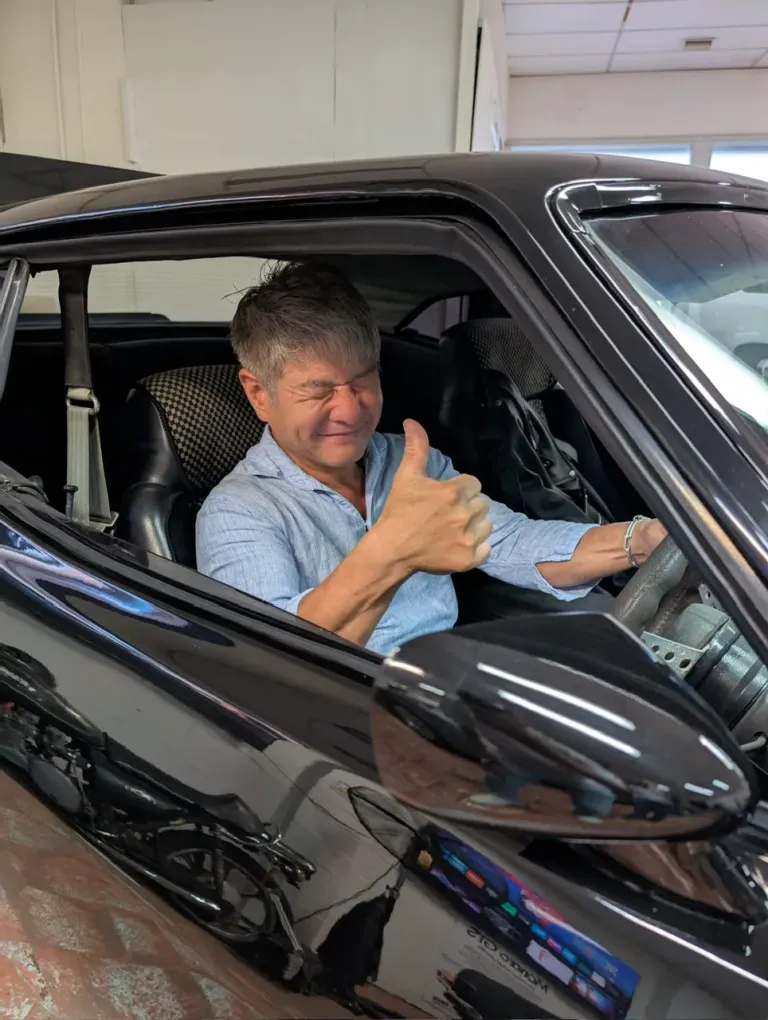 Smiling man giving a thumbs up from the driver's seat of a black car