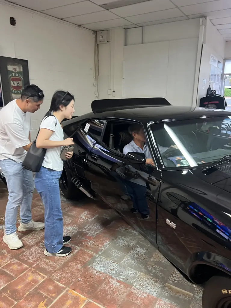 Two visitors look on as a man sits in the driver's seat of the black Interceptor replica